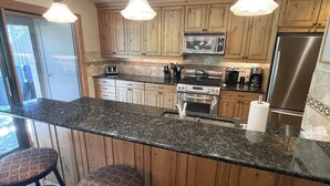 Una cocina con armarios de madera, un refrigerador de acero inoxidable, un microondas, una estufa y una isla grande con taburetes de bar.