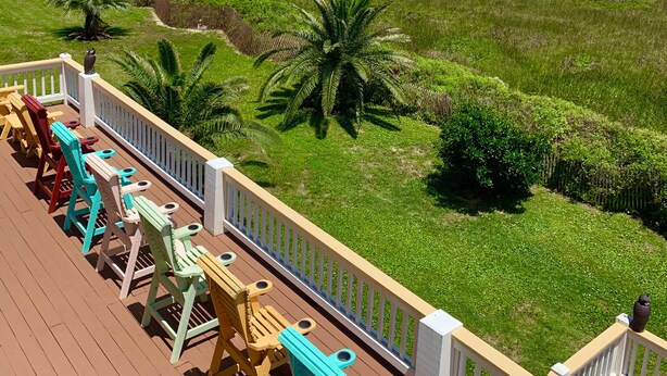 Une terrasse agrémentée de chaises et de tables colorées, donnant sur une plage et sur une promenade en bois.