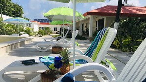 Un espace aménagé au bord de la piscine, avec des chaises longues, des parasols et un ananas posé sur une table.