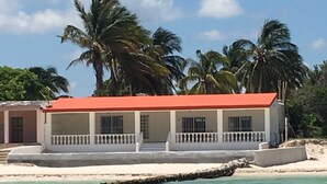 Un immeuble situé en bord de mer, avec un toit rouge, des murs blancs et un balcon.