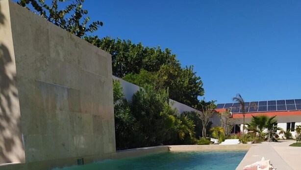Une table au bord de la piscine avec un verre contenant un liquide bleu, une assiette de mangues et de chocolat, et des coquillages.