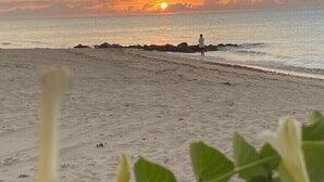 Une scène de plage au coucher du soleil, avec un promontoire rocheux et une personne debout près de l’eau.