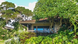 Una casa circondata da vegetazione lussureggiante e un cielo azzurro intenso.