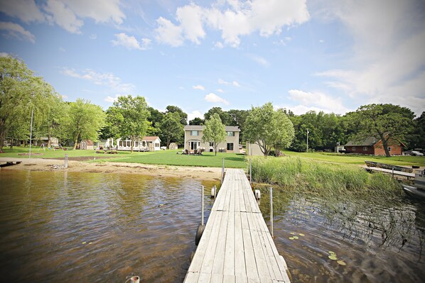 A wooden dock extending into a calm body of water, surrounded by lush greenery and a clear sky.