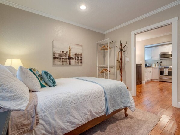Un dormitorio con una cama, una mesita de noche, una lámpara, un perchero y un cuadro de un paisaje urbano.