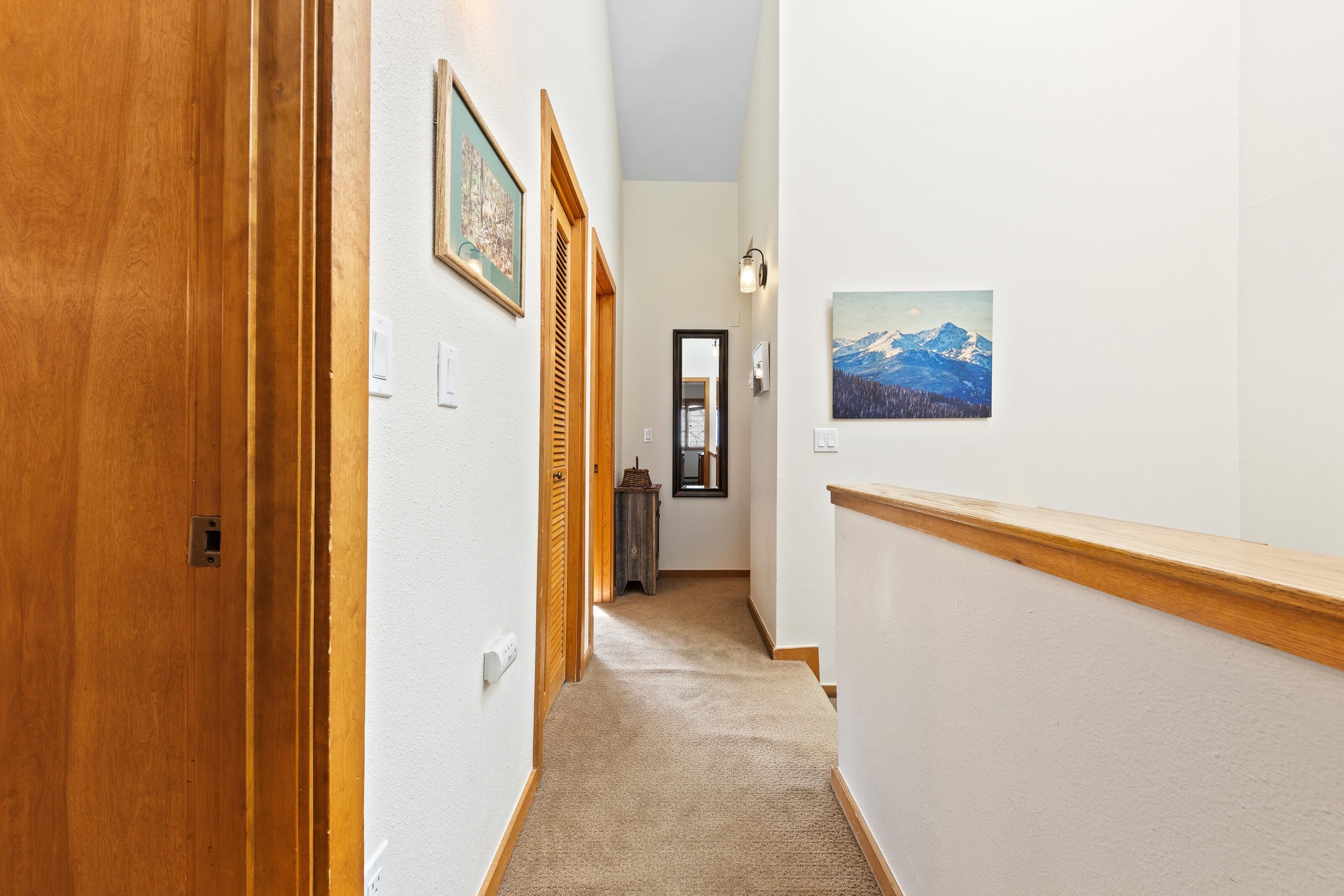 A hallway with wooden doors, a carpeted floor, and a painting of a mountain landscape on the wall.