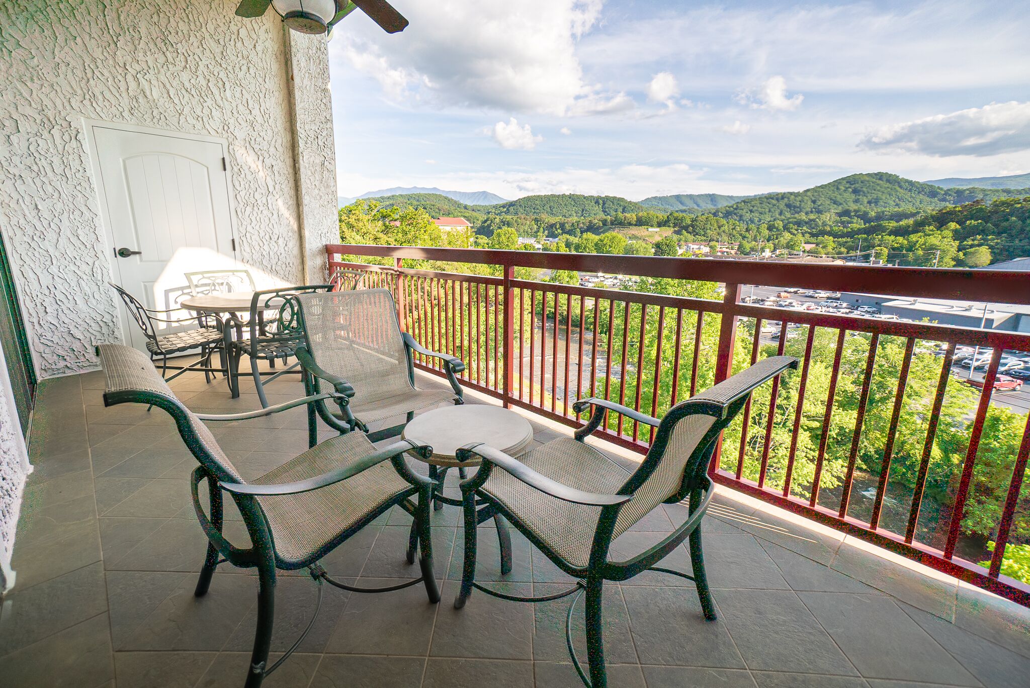 Un balcone con tavolo e sedie, una porta bianca e vista su colline verdi e un parcheggio.