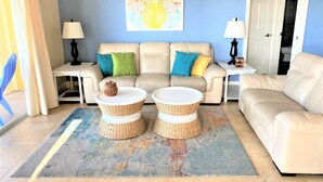 A living room with a beige sofa, two round wicker tables, a colorful abstract painting, and a blue wall. - Fantastic Gulf View! On the beach! 3 Bdrms, 3 Baths, Great Pool and Hot Tub (Redington Shores)