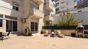 An outdoor patio area with tiled flooring, outdoor seating, potted plants, and a barbecue grill. - Graça House - Apartment T1 (Lisboa)