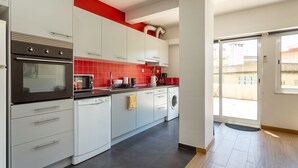 A modern kitchen with white cabinets, a black oven, and red-tiled backsplash. - Graça House - Apartment T1 (Lisboa)