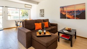 A modern living room with a brown sofa, a coffee table, and a cityscape painting on the wall. - Graça House - Apartment T1 (Lisboa)