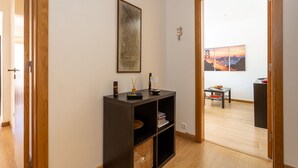 A hallway with a wooden door, a dark wooden console table with a framed picture, a small table with a basket, and a wall-mounted telephone. - Graça House - Apartment T1 (Lisboa)