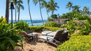 A beachside lounge with lounge chairs and a table, palm trees, and a view of the ocean.