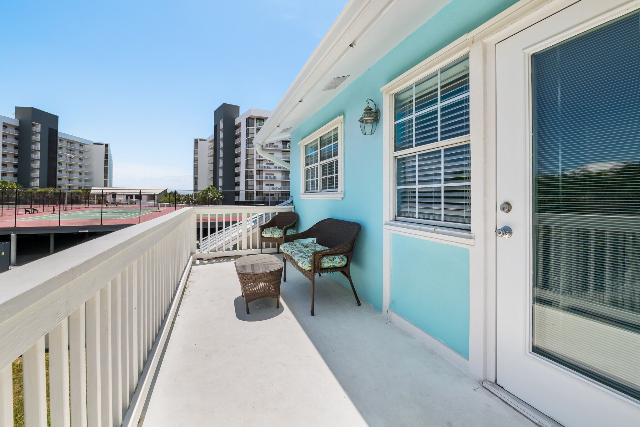 A balcony with wicker furniture, a door with a window, and a view of a sports court.
