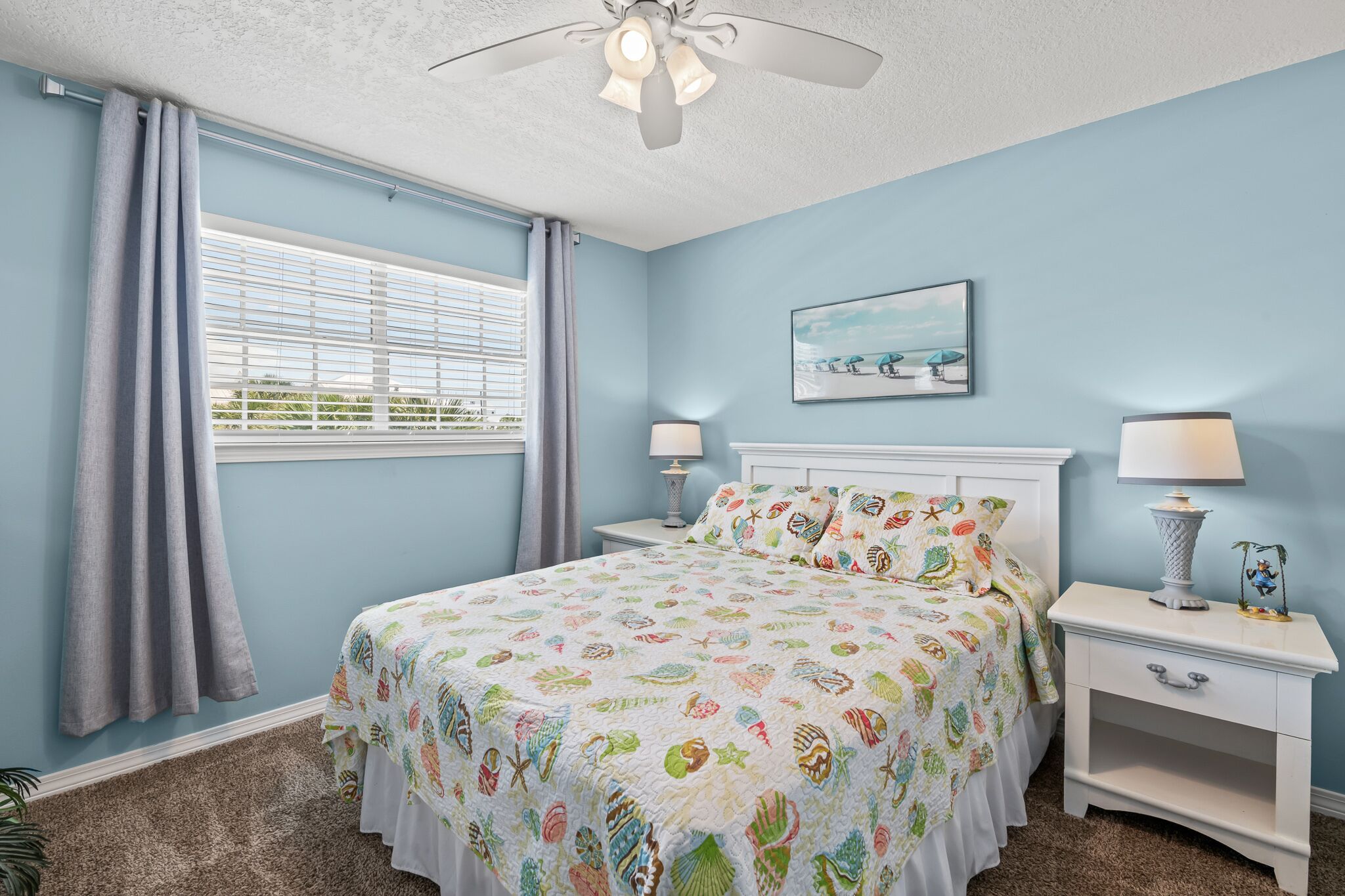 A bedroom with a bed, two nightstands, a ceiling fan, a window with curtains, and a painting on the wall.