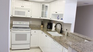 A kitchen with white cabinets, a built-in microwave, a stove, a sink, and granite countertops. - 5 Star Marco Island Beachfront Condo – Limited-Time Deals Available! (Marco Island)