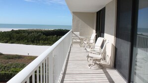 A balcony with a view of the beach, white chairs, and a glass door. - 5 Star Marco Island Beachfront Condo – Limited-Time Deals Available! (Marco Island)