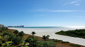 A beach with a clear view of the ocean, a road curving through the landscape, and a distant city skyline. - 5 Star Marco Island Beachfront Condo – Limited-Time Deals Available! (Marco Island)