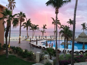 A resort pool area with palm trees, lounge chairs, and a view of the ocean. - Ocean view, one bedroom, steps to the pool and beach.  Pride in ownership. (San Jose del Cabo)