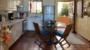 A kitchen with white cabinets, a refrigerator, a coffee maker, and a dining table with chairs. - Ocean view, one bedroom, steps to the pool and beach.  Pride in ownership. (San Jose del Cabo)