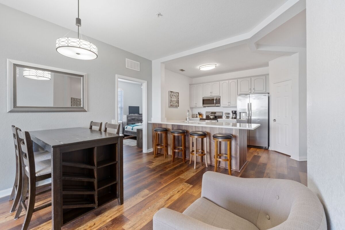 A modern kitchen with white cabinets, a central island with stools, and a dining area with a wooden table and chairs.