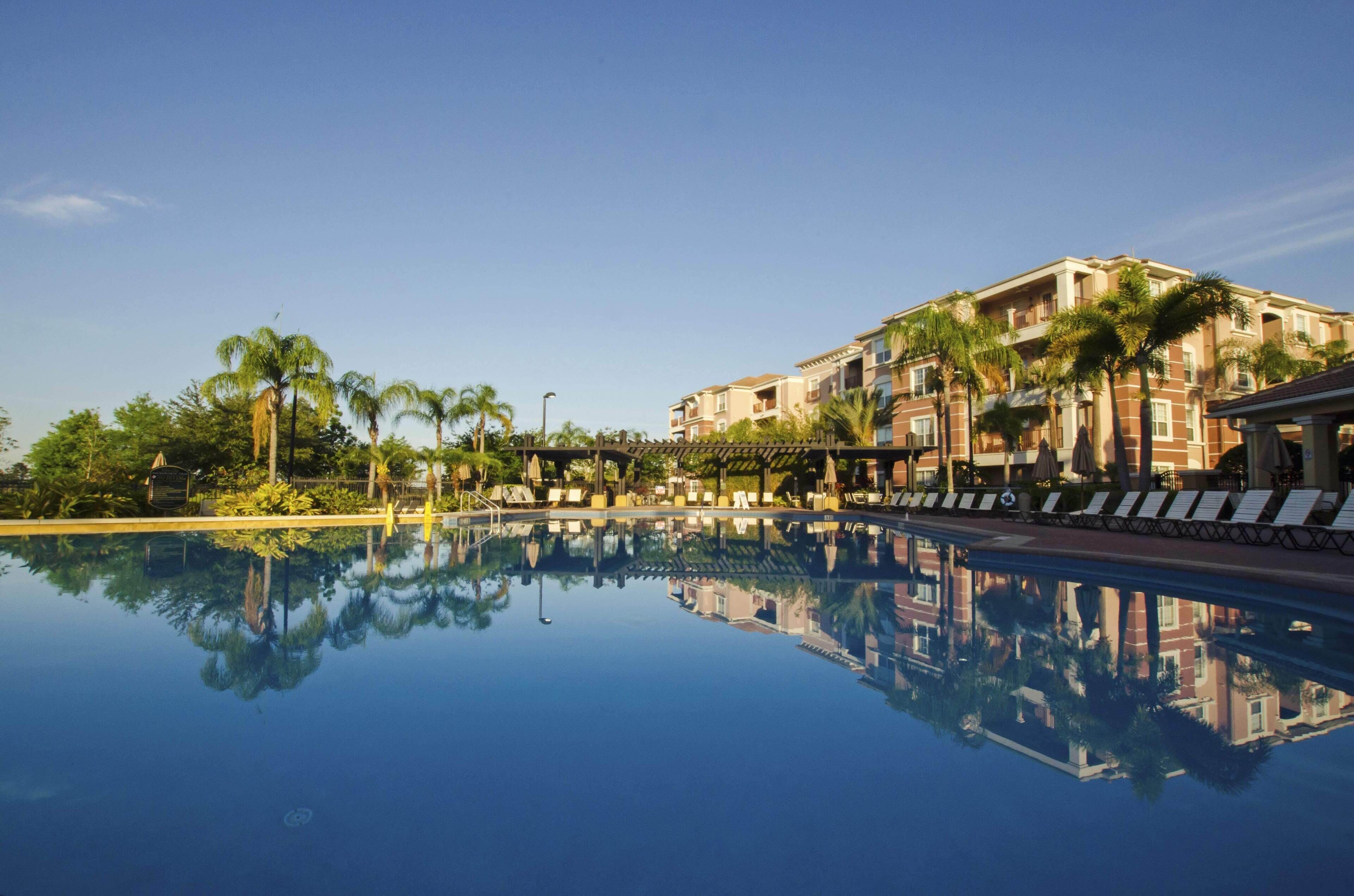 A hotel with a pool reflecting palm trees and a building with balconies.