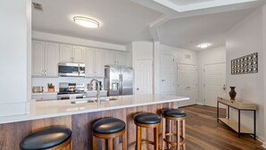 Cozinha moderna com armários brancos, eletrodomésticos de aço inoxidável, ilha de madeira com banquetas e piso de madeira.