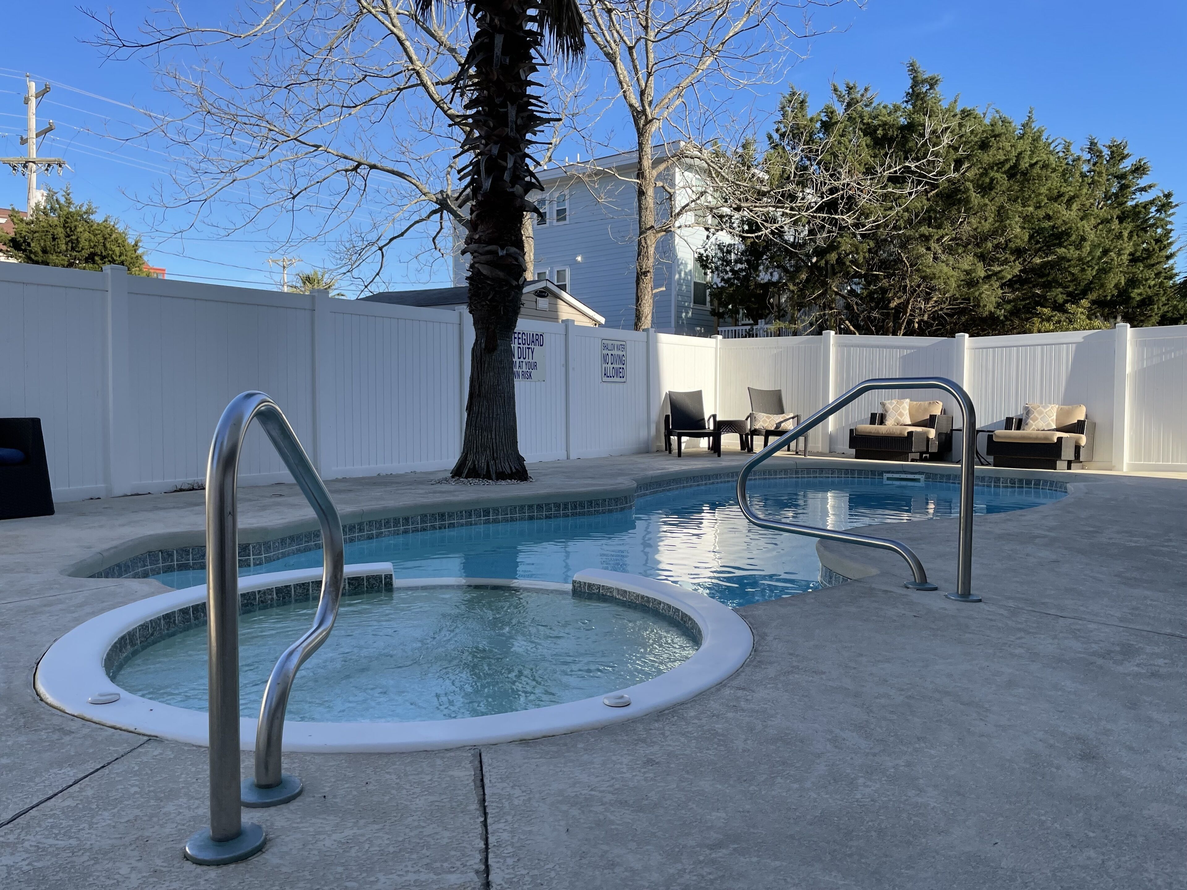A swimming pool with a metal ladder, surrounded by a white fence, and a tree in the background.