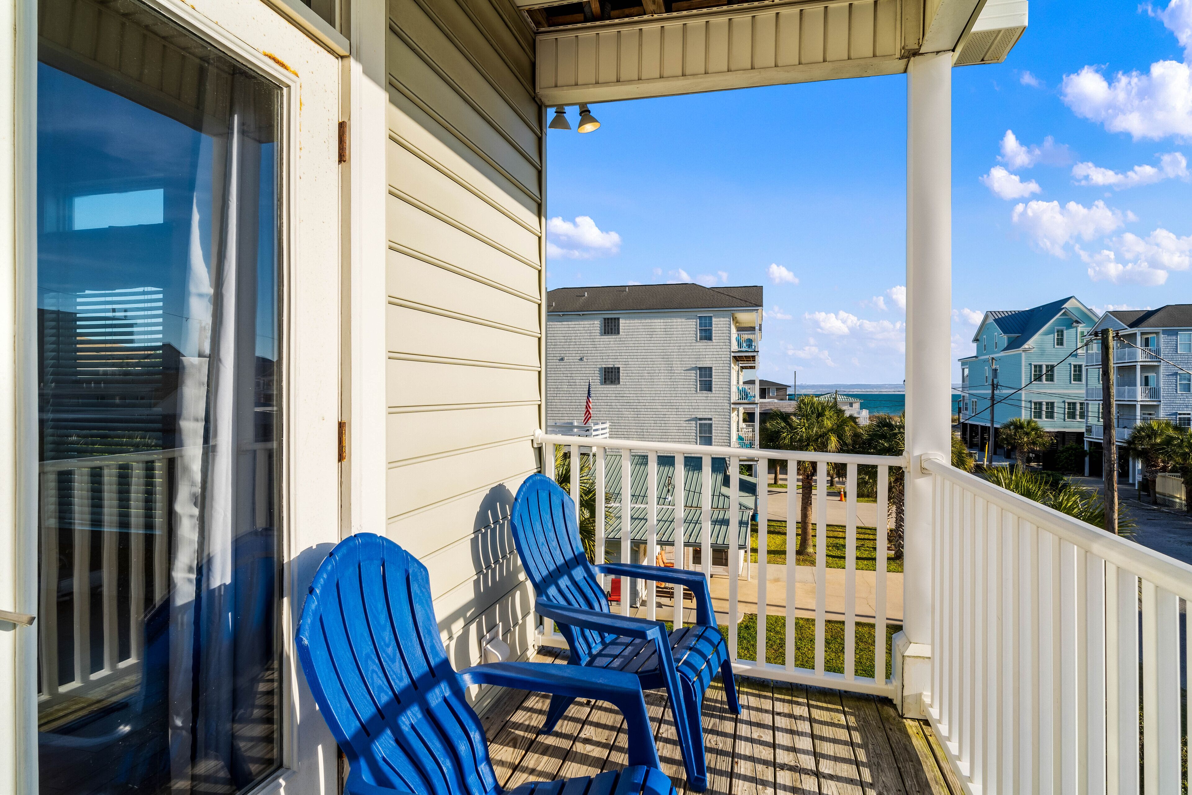 Un balcon avec deux fauteuils Adirondack bleus, une balustrade blanche et une vue sur d’autres immeubles et l’oc éan.