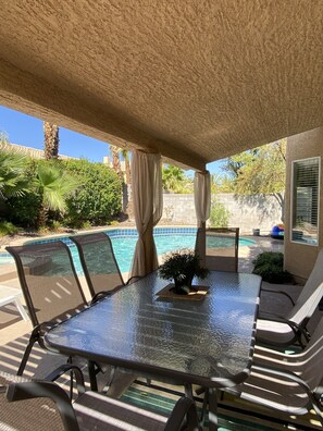 An outdoor patio with a glass table and chairs, a pool, and a covered area with a textured ceiling. - Families! Get-a ways! Private Home! - Pool! Billiard Table! Couples! Golfers! (Henderson)