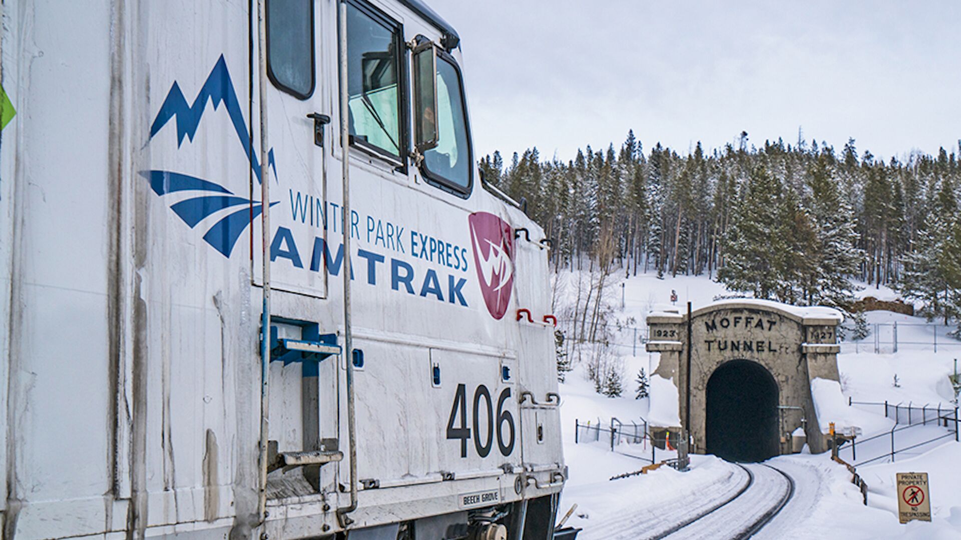 A white truck with "Winter Park Express" and "AMTRAK" logos, parked near a snow-covered tunnel entrance.