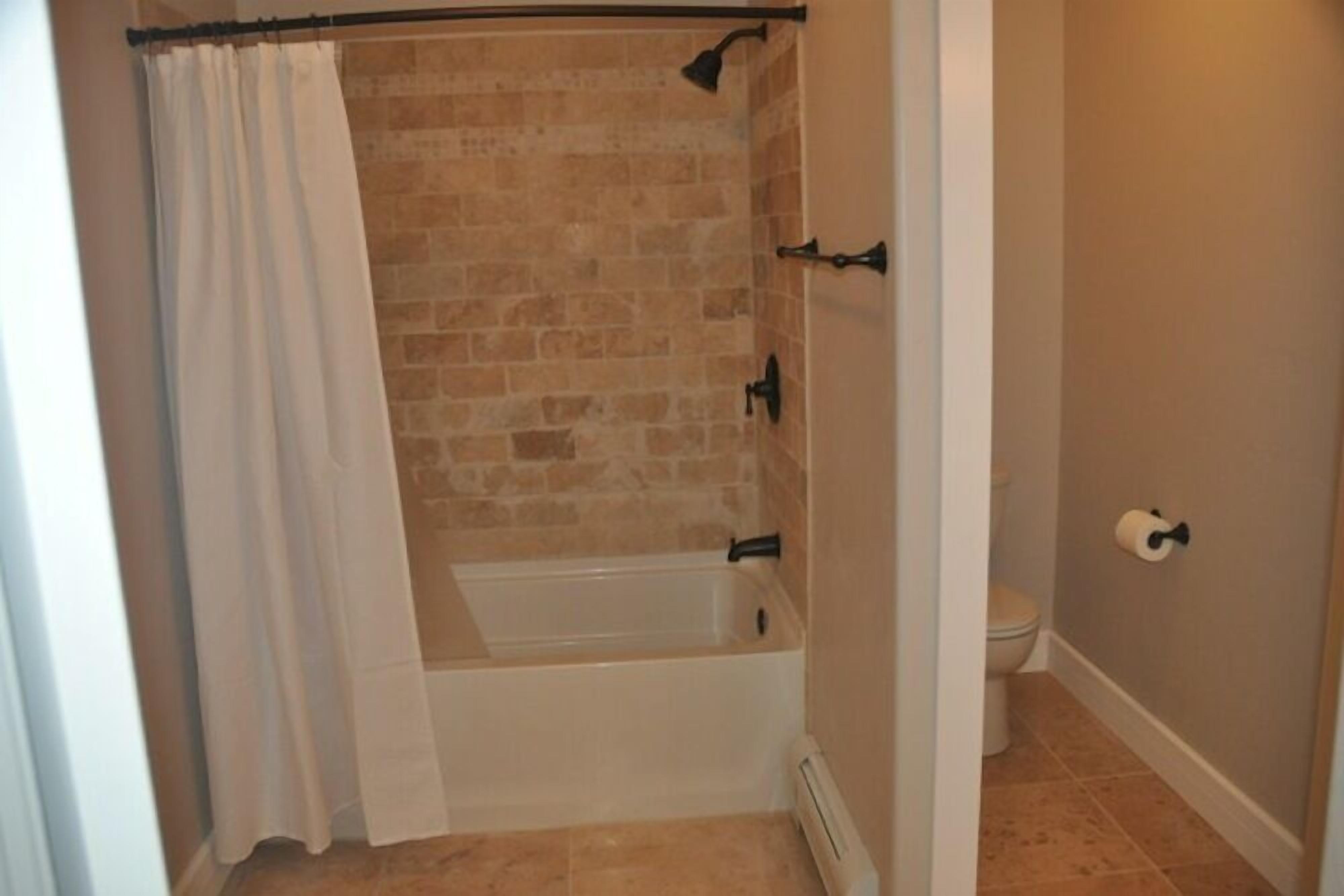 A bathroom with a brick wall, a bathtub, a toilet, and a shower curtain.