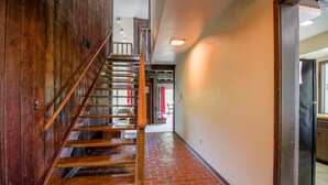 Un escalier en bois menant à l’étage supérieur, un plancher en briques et un coin cuisine avec des placards et un réfrigérateur.