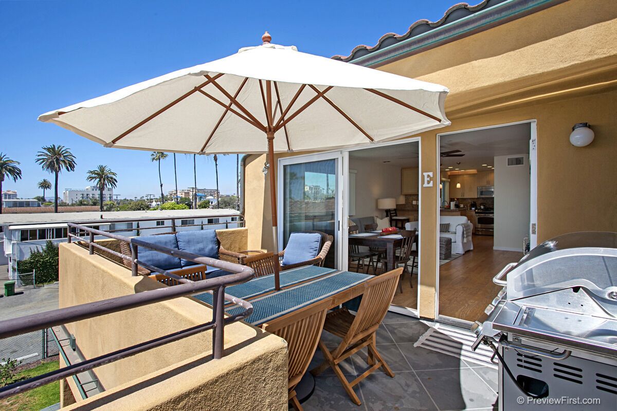 A balcony with wicker furniture, a grill, and a view of palm trees and buildings.