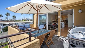 A balcony with wicker furniture, a grill, and a view of palm trees and buildings. - OCEANSIDE BEACH located by pier and marina! Ocean Views! Walk to Village! (Oceanside)
