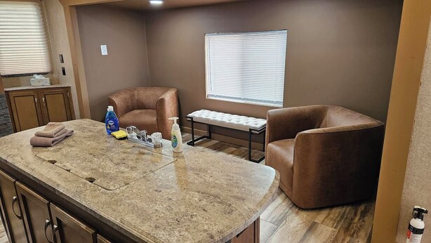 A compact kitchen with a central island, a dining table, and two brown leather chairs. - Catalina Park Model, in RV Ballard RV Park  (Thompson)
