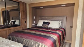 A bedroom with a bed, a wooden headboard, and a large mirror. - Catalina Park Model, in RV Ballard RV Park  (Thompson)