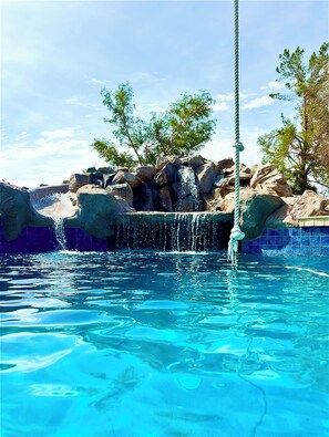 A clear pool with a waterfall feature, surrounded by rocks and trees.