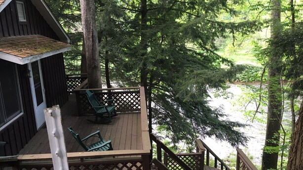 A wooden deck with a view of a forest and a body of water. - Pine Creek Treehouse (Gaines)