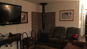 A living room with a stone fireplace, a flat-screen TV, a sofa, and a chair. - Pine Creek Treehouse (Gaines)