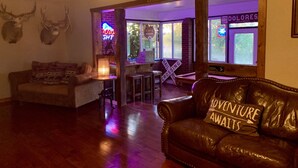 A cozy living room with a leather couch, a wooden coffee table, and a fireplace. There are deer antlers on the wall and a neon sign. - LUXE Lodge 80ac. Huge pond cattle Ranch Views Close Nat Parks Ski McPhee (Dolores)