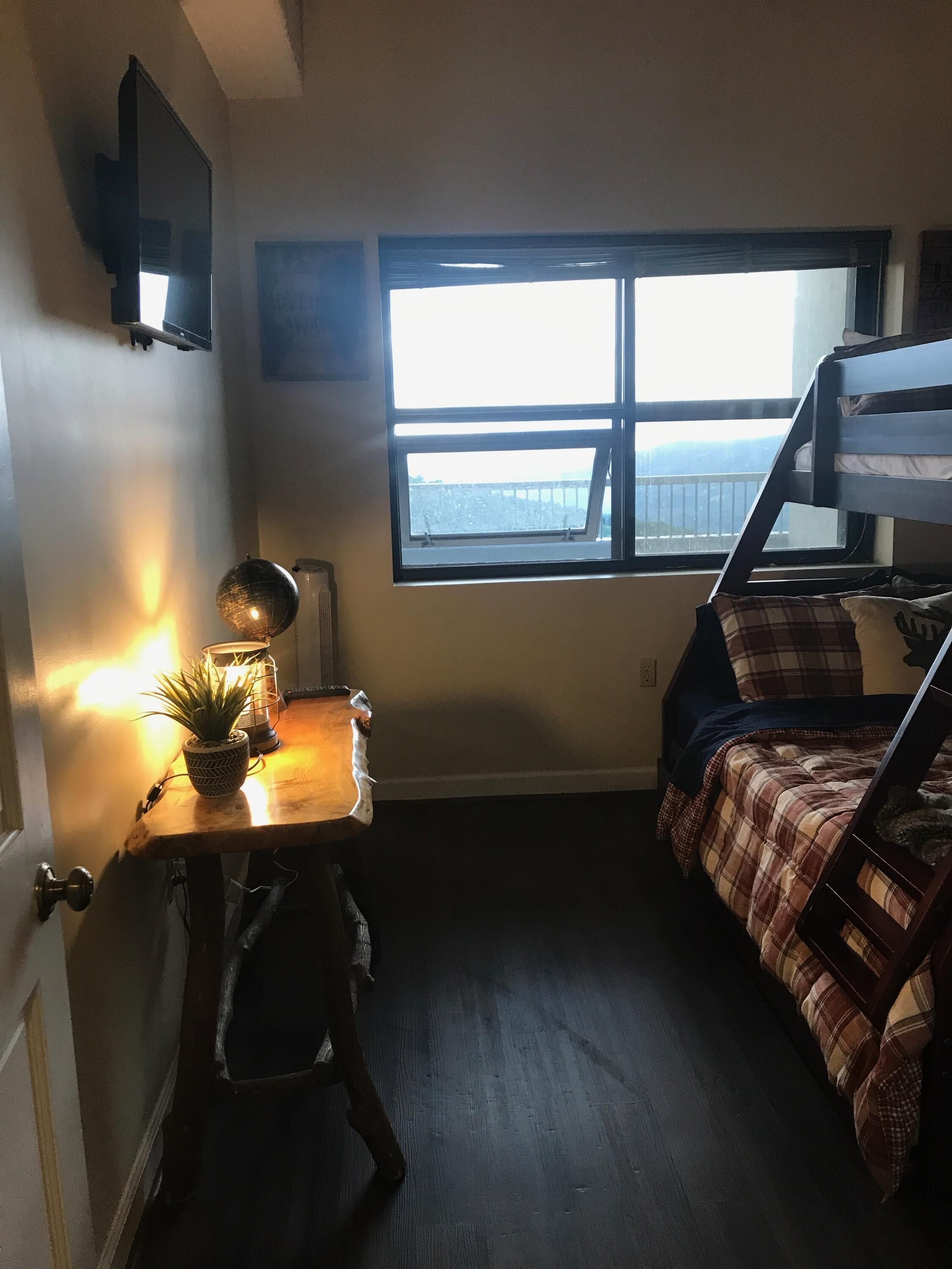 Et lille værelse med køjeseng, et skrivebord med lampe og et vindue med udsigt.