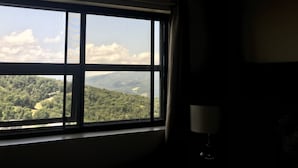 A room with a large window offering a view of a forested landscape. - Spectacular Mile High View,Free Wifi-Pool-Smart Tvs-W&D-Gym-No hidden fees ! (Banner Elk)