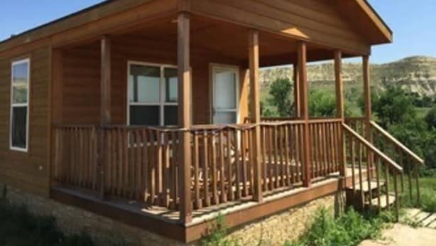 Une cabane en bois dotée d’une véranda, de fenêtres et offrant une vue sur le paysage environnant.