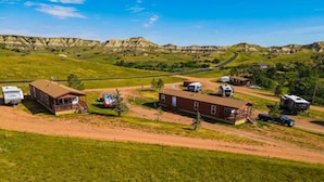 Un terrain de camping pour véhicules récréatifs situé en zone rurale, avec plusieurs véhicules récréatifs, un bâtiment en briques et un chemin de terre.