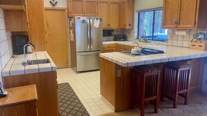 A kitchen with wooden cabinets, a stainless steel refrigerator, a microwave, and a large island with stools. - Ebbetts Pass Getaway - Awesome Easy Access Large Mountain Cabin (Arnold)