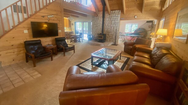 A spacious living area with a stone fireplace, leather furniture, and a wooden staircase. - Ebbetts Pass Getaway - Awesome Easy Access Large Mountain Cabin (Arnold)