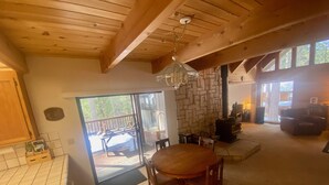 A cozy interior with a wooden dining table, a stone fireplace, and a balcony with a wooden deck. - Ebbetts Pass Getaway - Awesome Easy Access Large Mountain Cabin (Arnold)