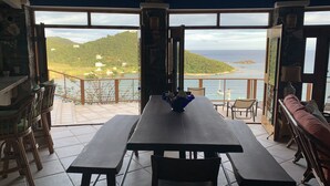 A dining area with a table and benches, a sofa, and a view of a coastal landscape.