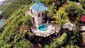 A house with a pool surrounded by lush greenery and a view of the sea.